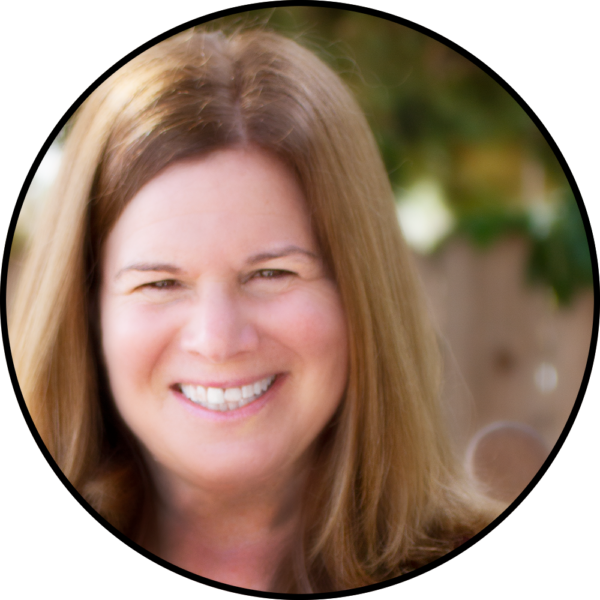 A smiling woman with long brown hair, outdoors in soft natural light.